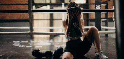 A female boxer sitting in a gym ring, resting and wiping sweat with a towel after a workout.